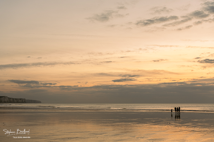 Promeneurs sur la plage d'Ault au soleil couchant
